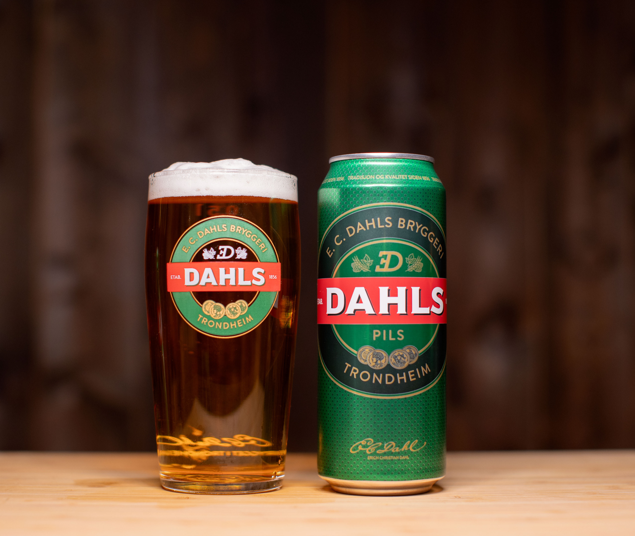 Et glass og en boks Dahls på bord foran mørk trebakgrunn.